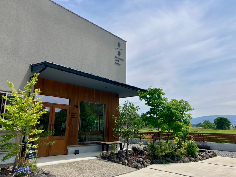 阿蘇の山並みを背景にしたsakurayama coffee roasterの外観と緑豊かな庭