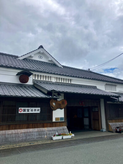 寛政蔵の白い外壁と木の扉、入り口前には色とりどりの花が並ぶ落ち着いた雰囲気の外観