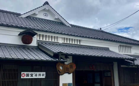 寛政蔵の白い外壁と木の扉、入り口前には色とりどりの花が並ぶ落ち着いた雰囲気の外観