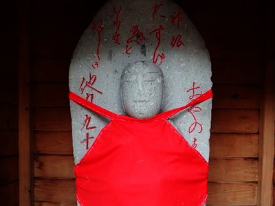 赤い前掛けをする放牛石仏